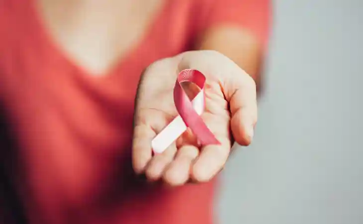 Woman in a red shirt holds out a pink breast cancer ribbon.