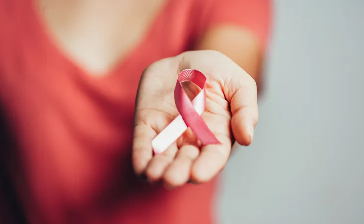 Woman in a red shirt holds out a pink breast cancer ribbon.