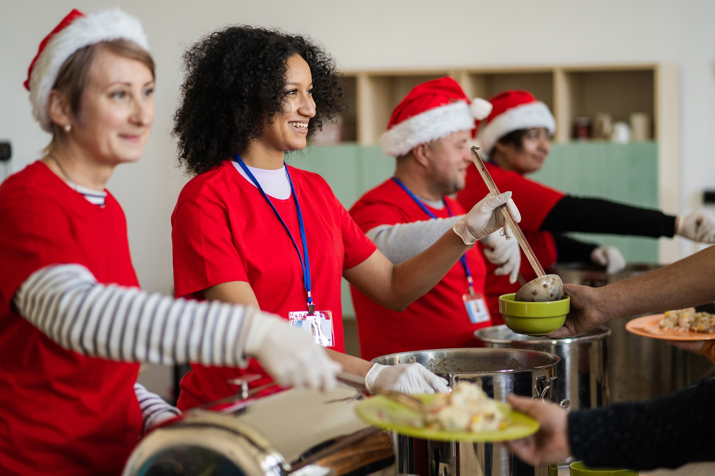 Four people in Christmas outfits serving a variety of food options to other people.