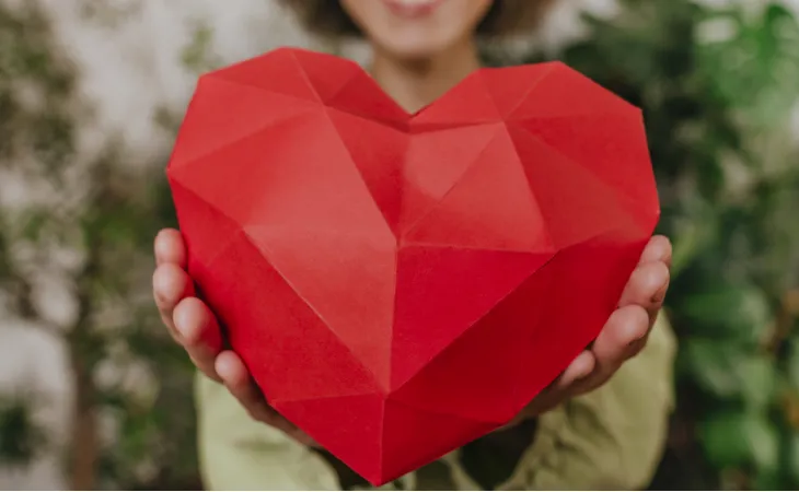 A woman holds a geometric sculpture heart out in front of her.
