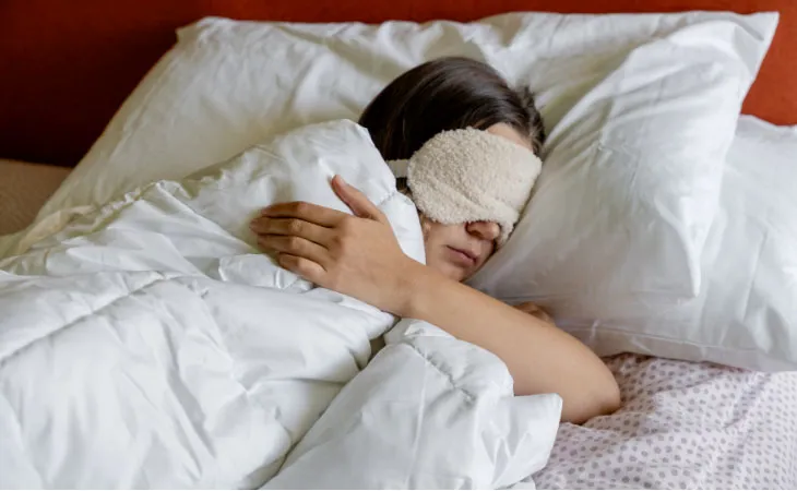 A young person resting in bed utilizing a sleep mask.
