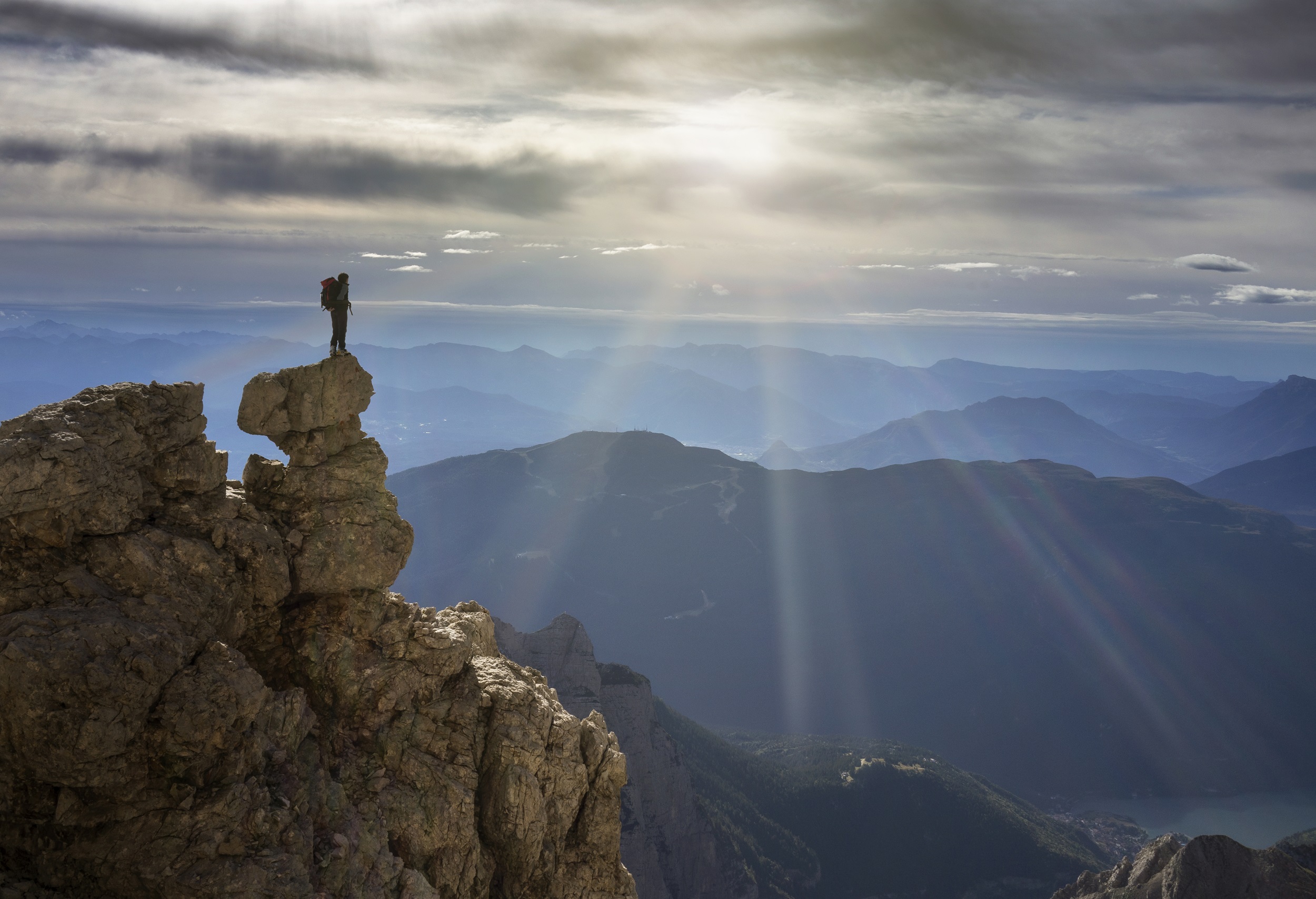 A person standing at the edge of a mountaintop, gazing at the panoramic view of surrounding mountains.