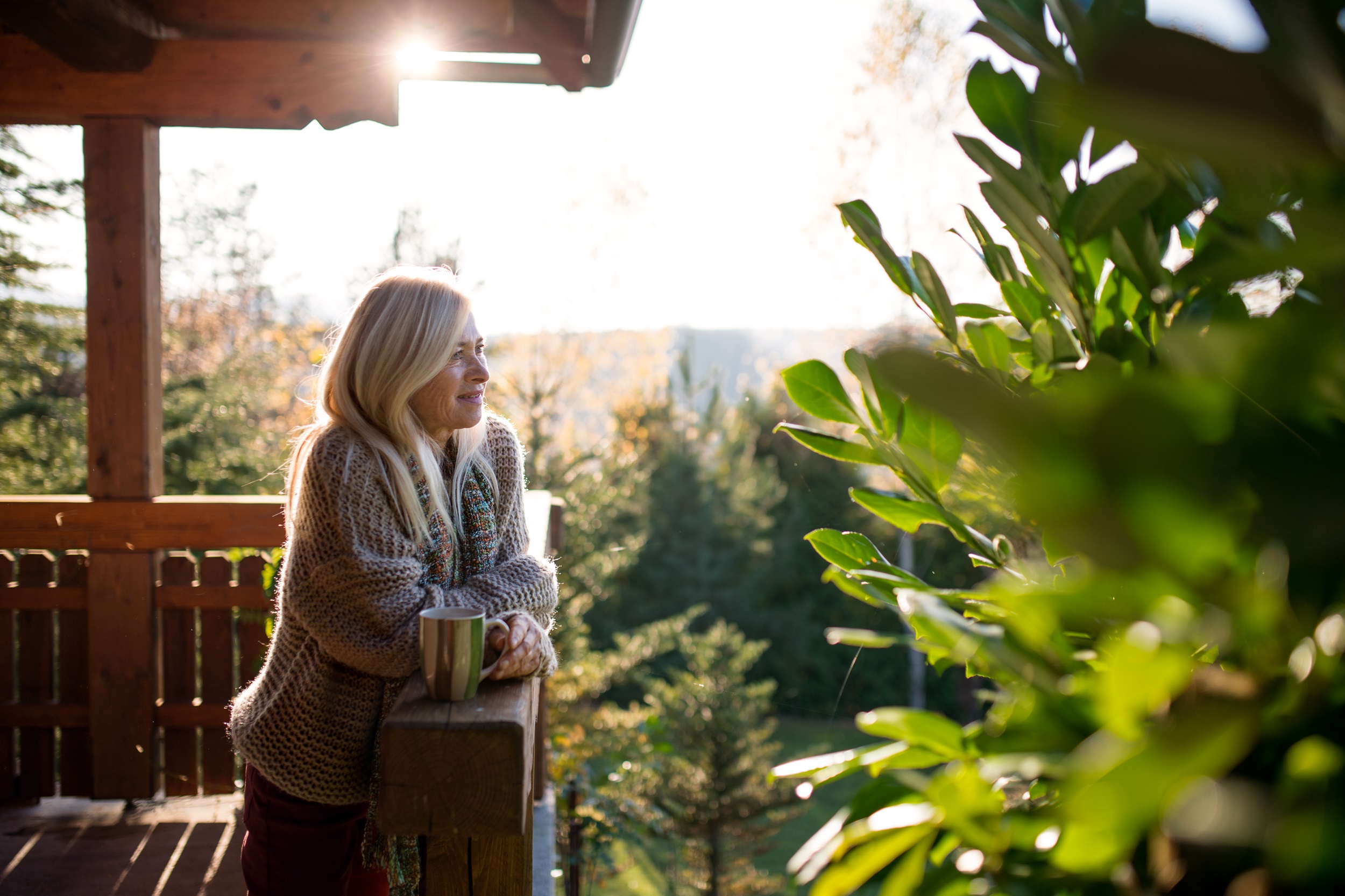A woman standing on her balcony, holding a cup of coffee and gazing at the view.