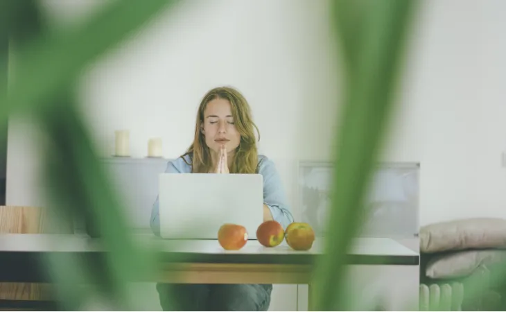 Woman meditating in front of laptop.