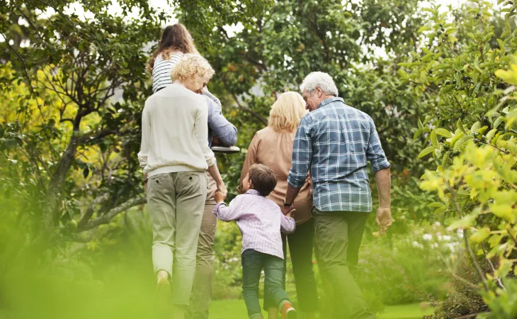 Multiple generations of a family walk through a lush wooded garden.
