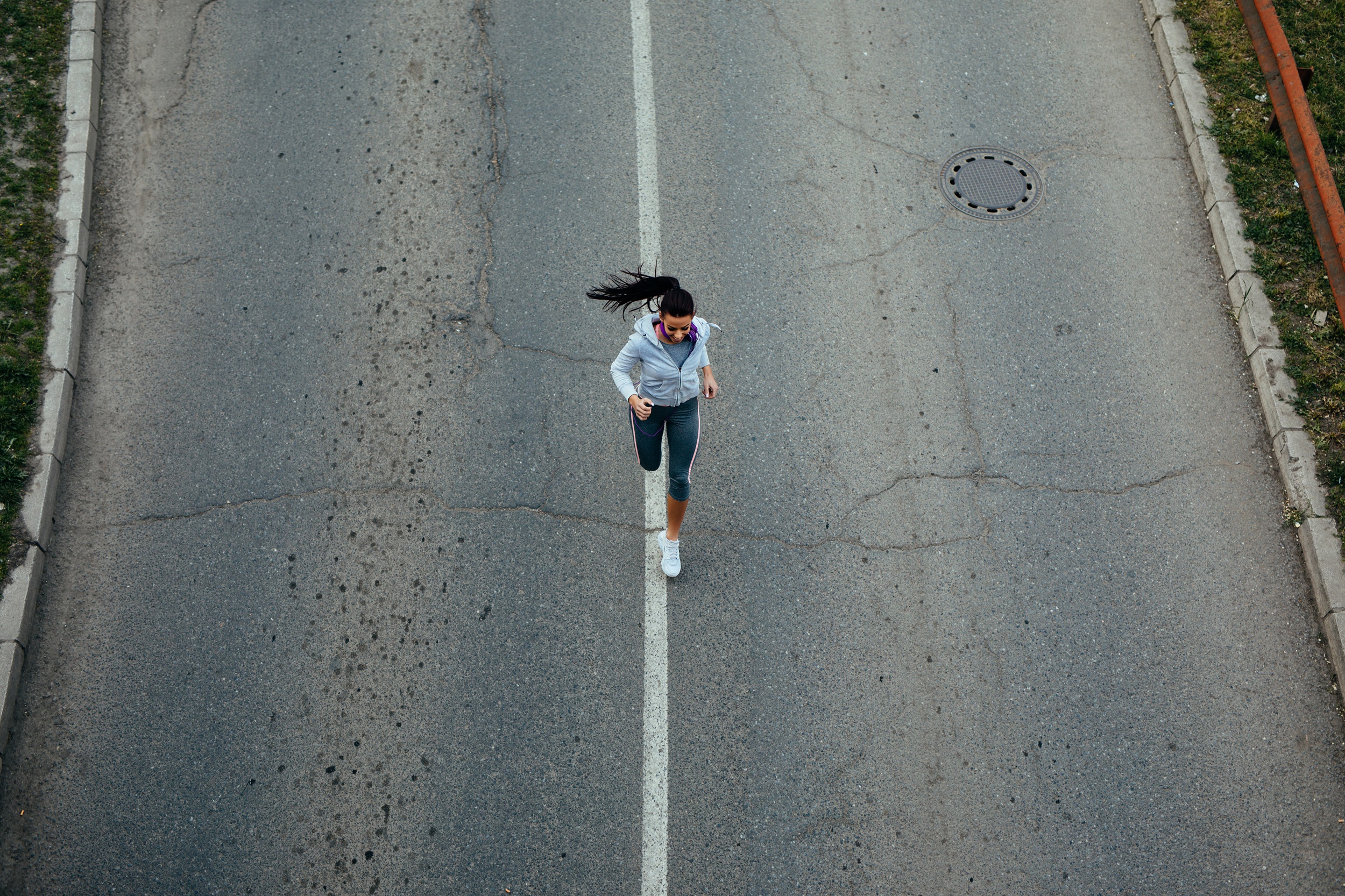 A woman with a ponytail running in a sporty outfit on an empty road.